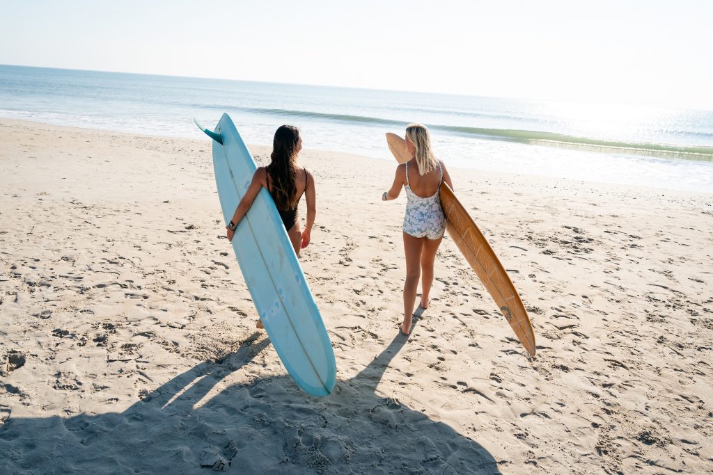 two women carrying longboard surfboards to the beach
