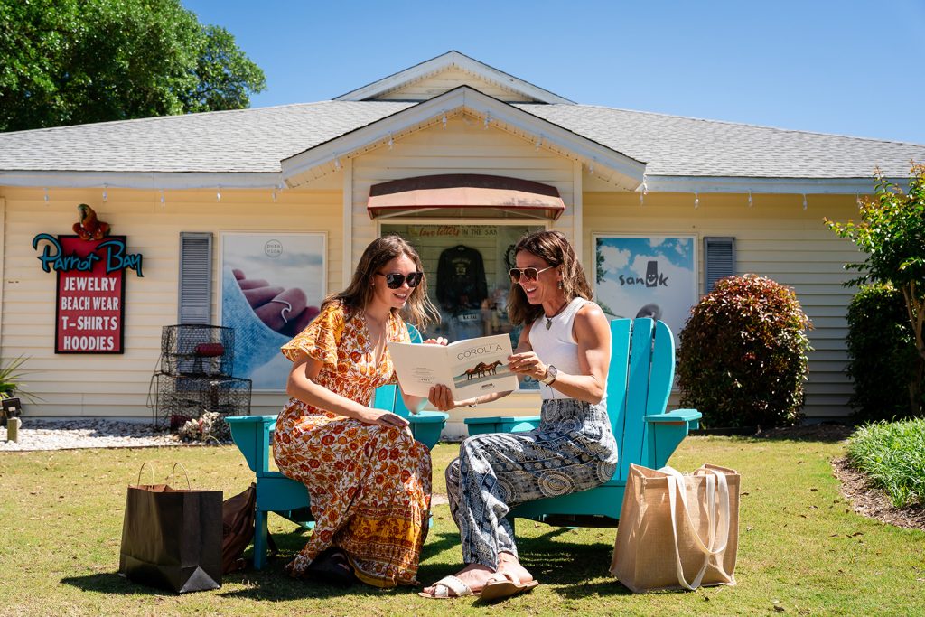 Two women sitting on Adirondack chairs outside a shop