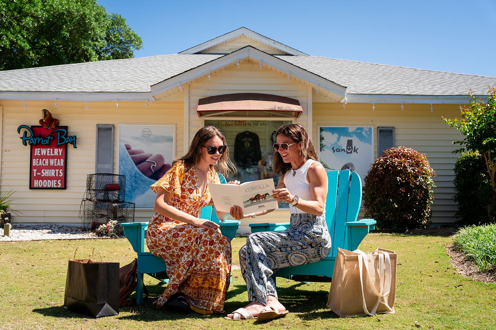 Two women sitting on Adirondack chairs outside a shop